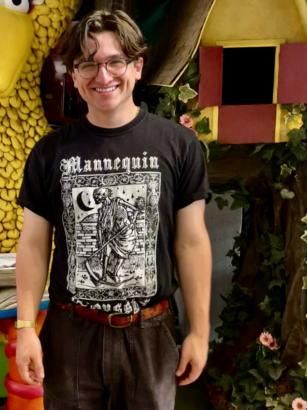 Thomas Costello smiling in a black Mannequin t-shirt in front of a carnival backdrop